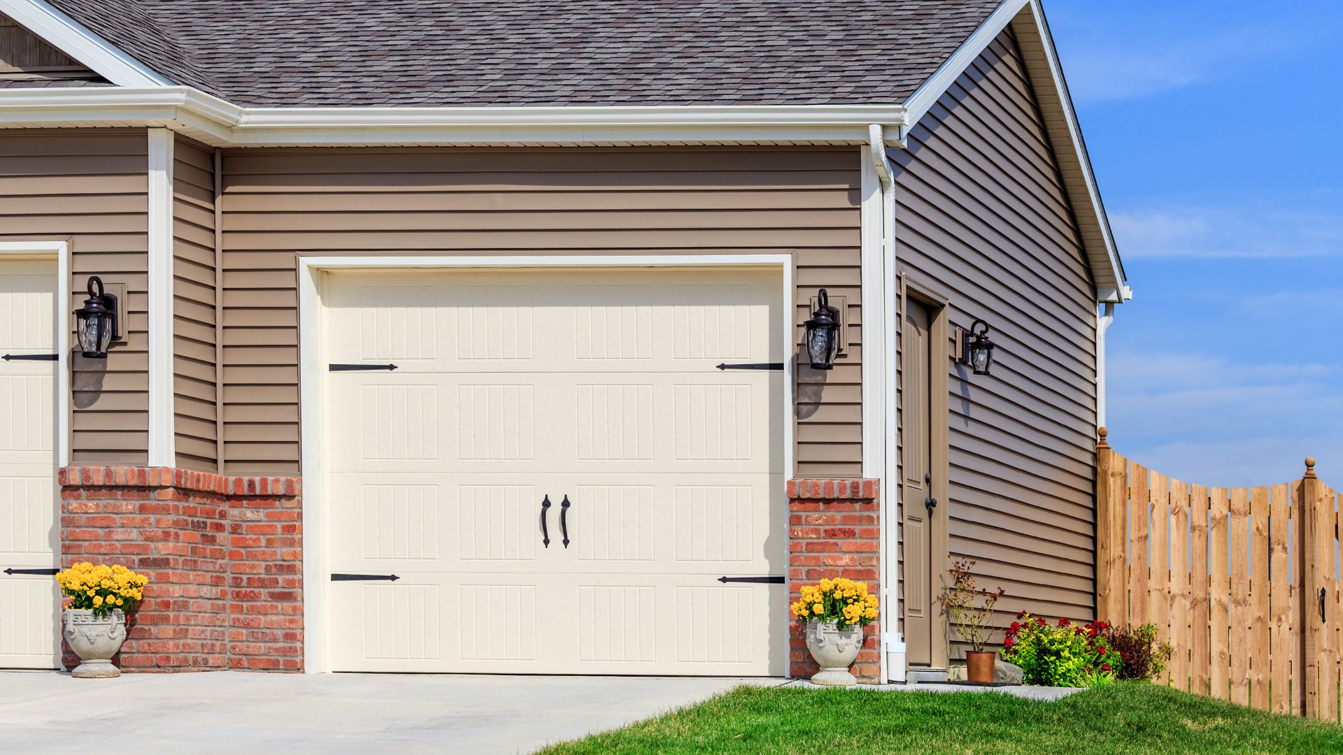 White garage door with brick accents and yellow flowers on sunny day