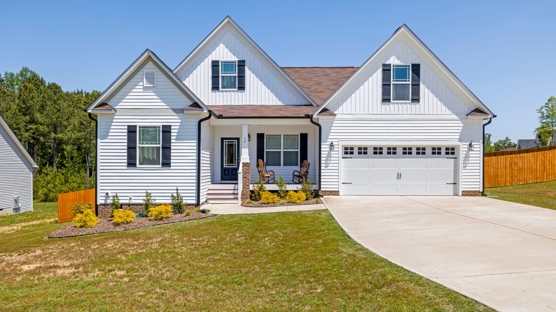 White two-story house with black shutters and two rocking chairs on porch