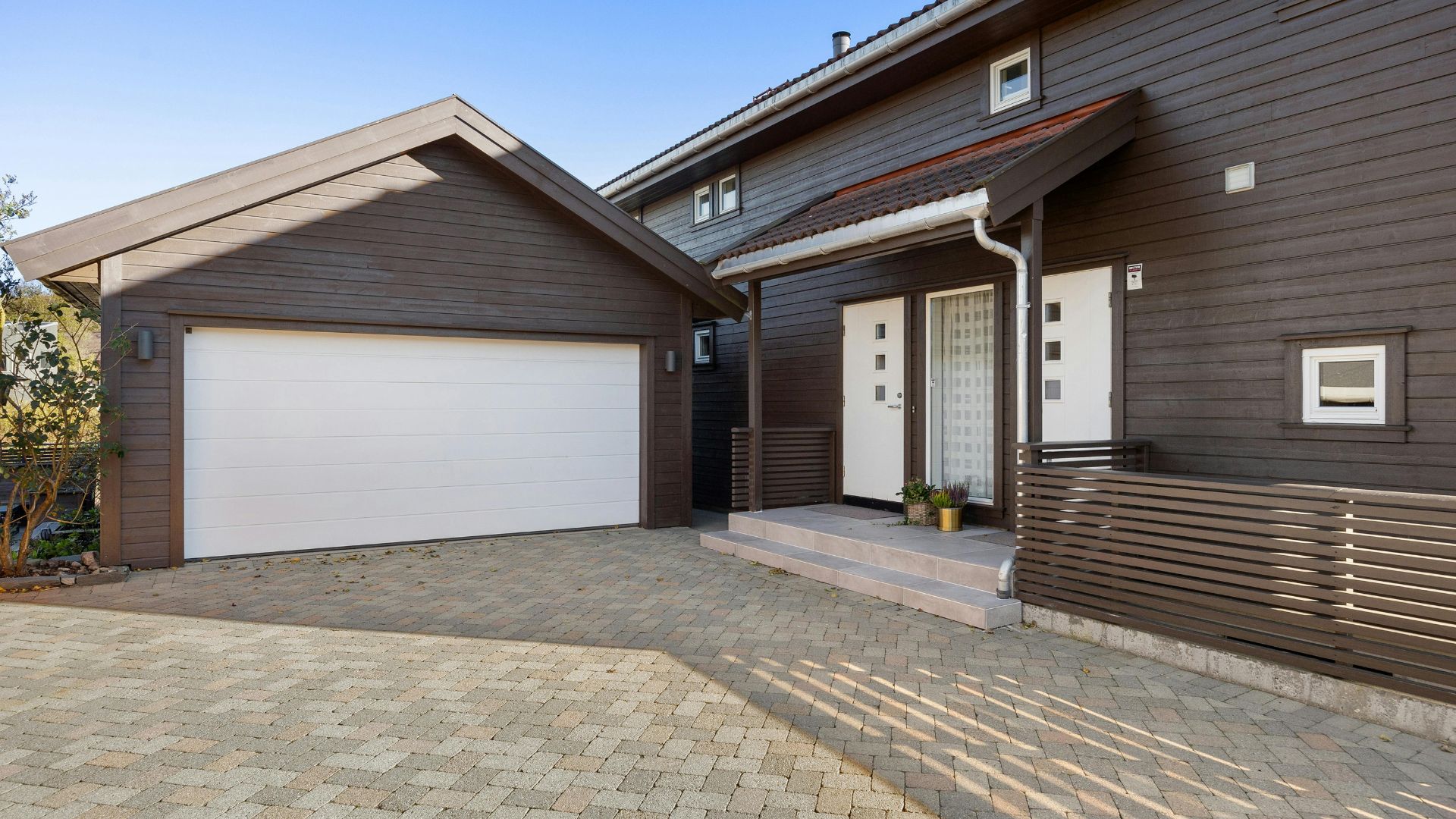 Modern house with white garage door, wooden siding, and paver driveway