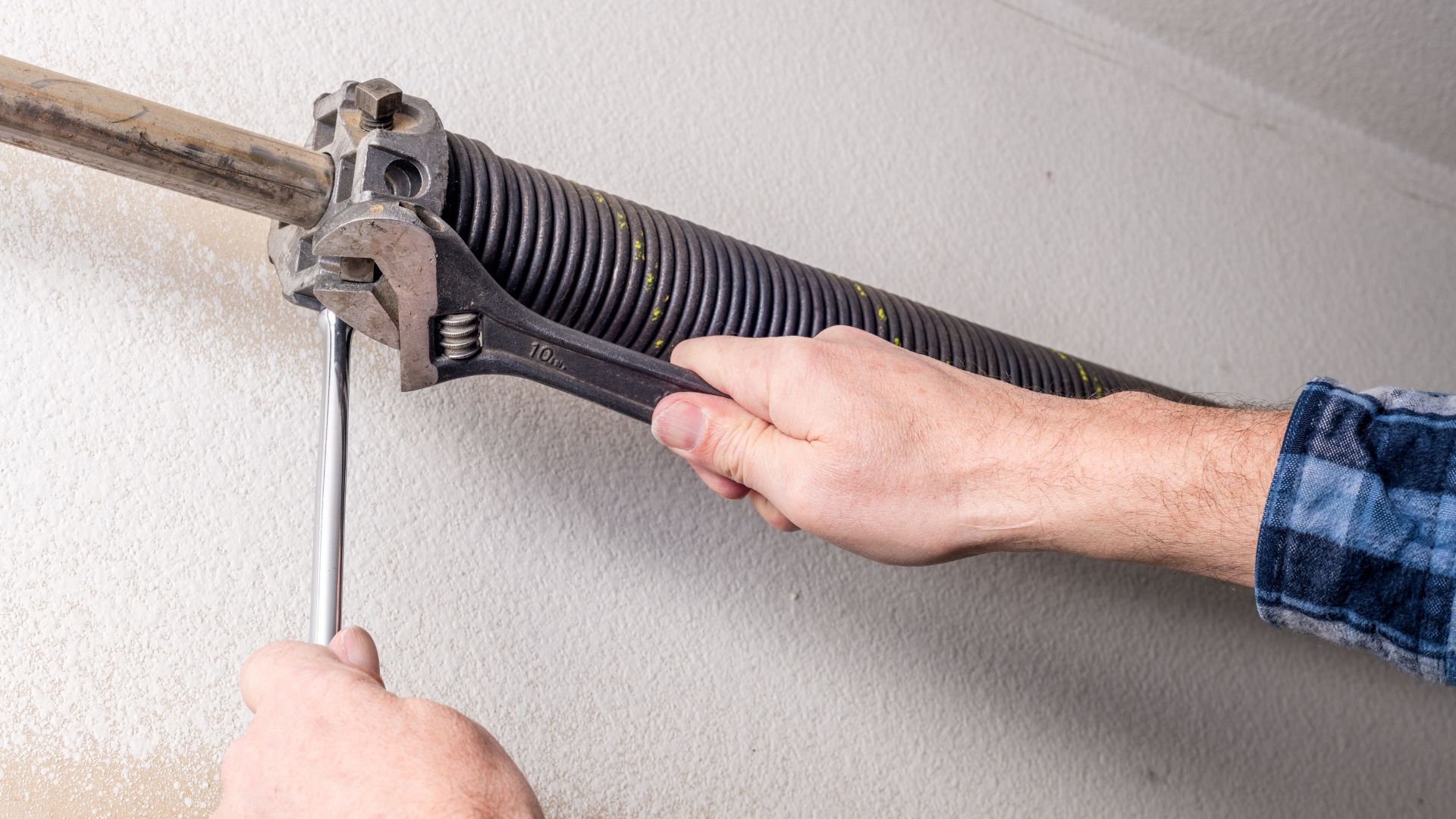 Hands adjusting garage door spring with wrench on white wall